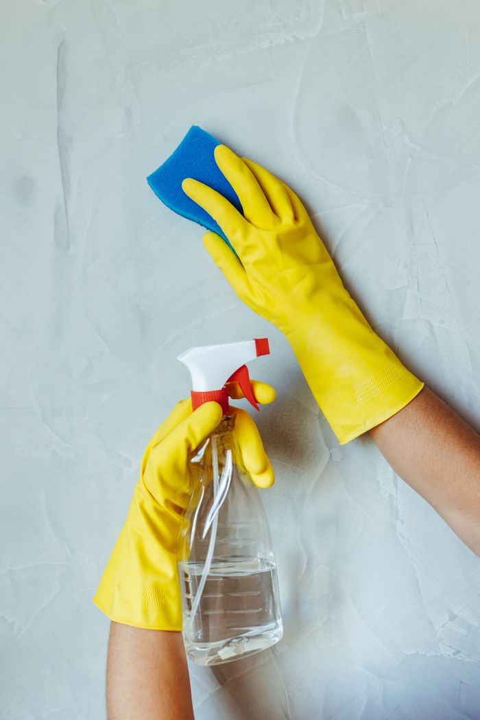about-us-02 Hands in yellow gloves cleaning wall with sponge and spray bottle.